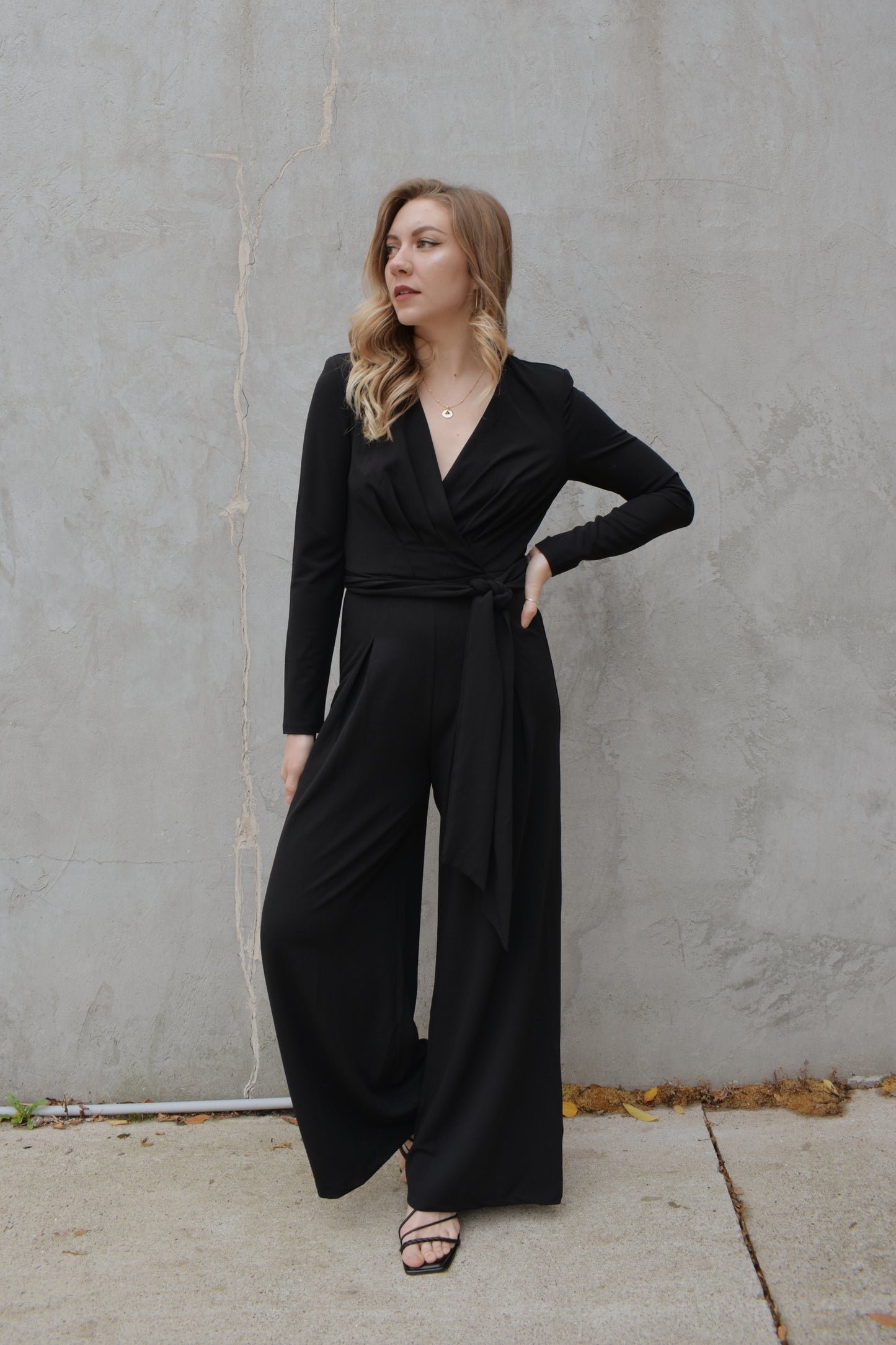 black wide leg long sleeve jumpsuit with wrap effect and fabric tie. pleated v neck with fitted arms and zip back enclosure