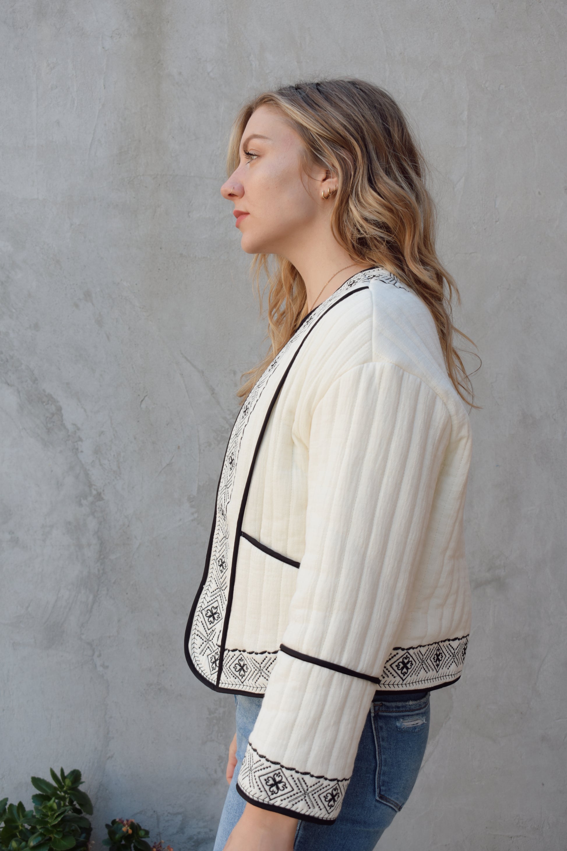 boho quilted ivory jacket with black exposed seam detailing and design along hem, has pockets, 2 clasp enclosure 