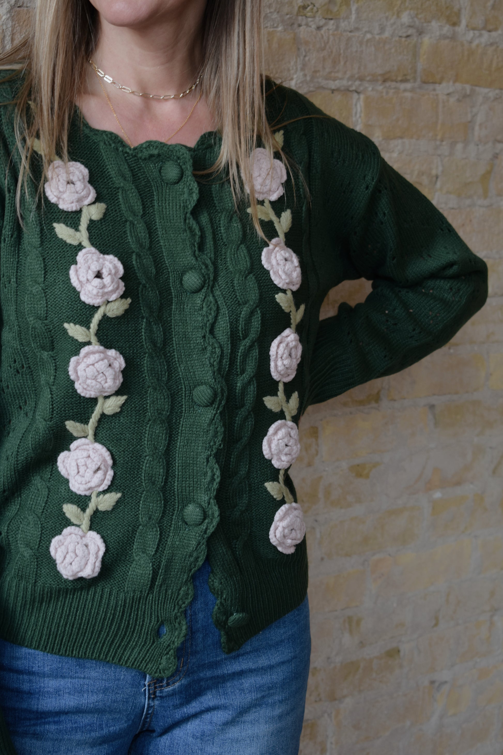 green cable knit cardigan with scalloped neckline, light pink flower crochet detailing along front ribbed cuffs and hem, hip length, relaxed fit