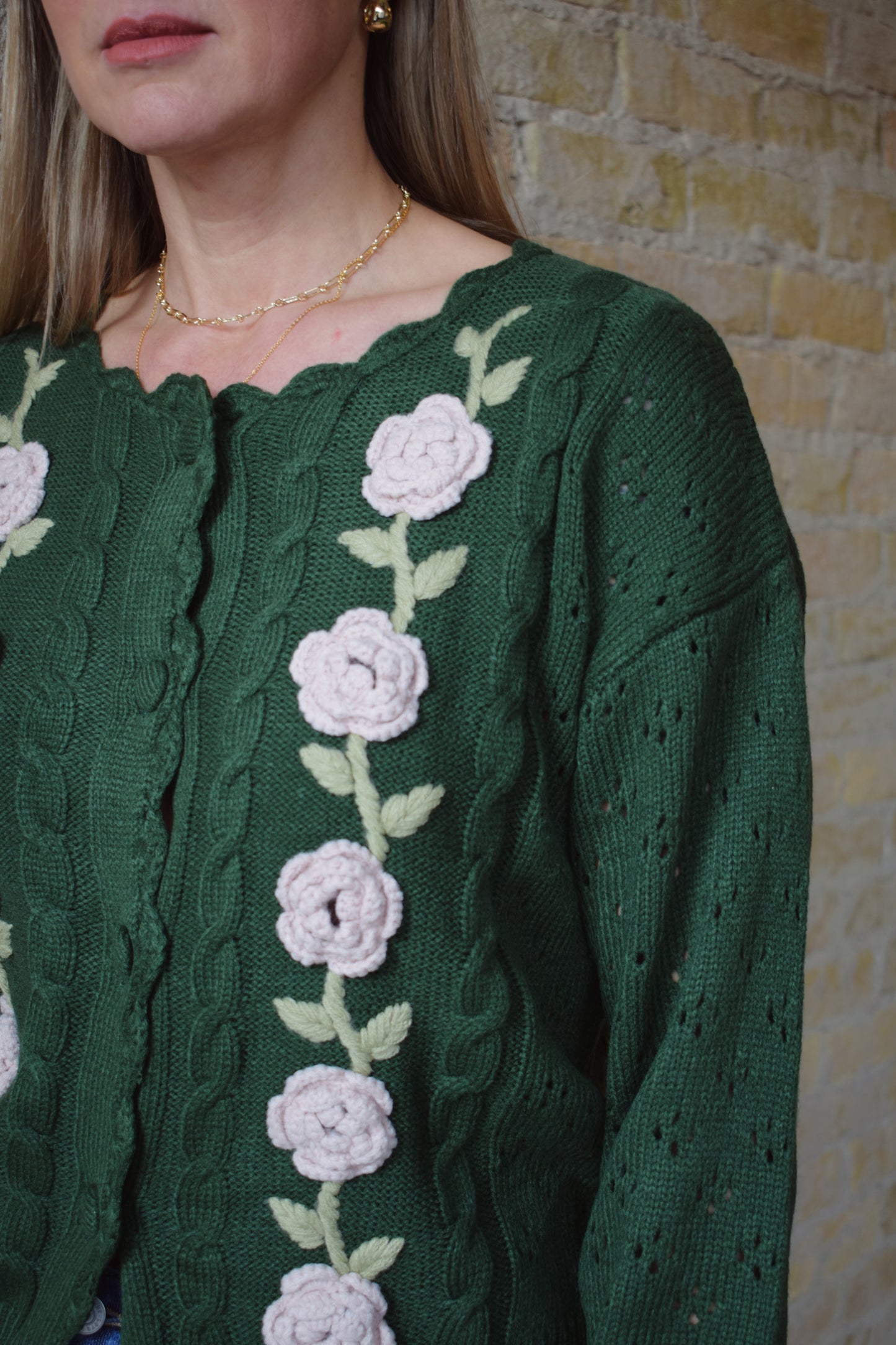 green cable knit cardigan with scalloped neckline, light pink flower crochet detailing along front ribbed cuffs and hem, hip length, relaxed fit