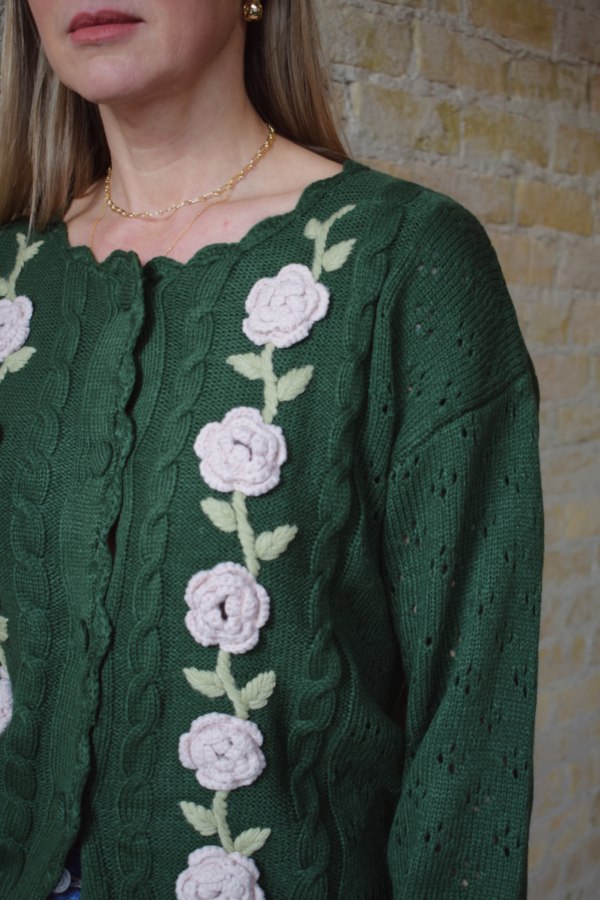 green cable knit cardigan with scalloped neckline, light pink flower crochet detailing along front ribbed cuffs and hem, hip length, relaxed fit