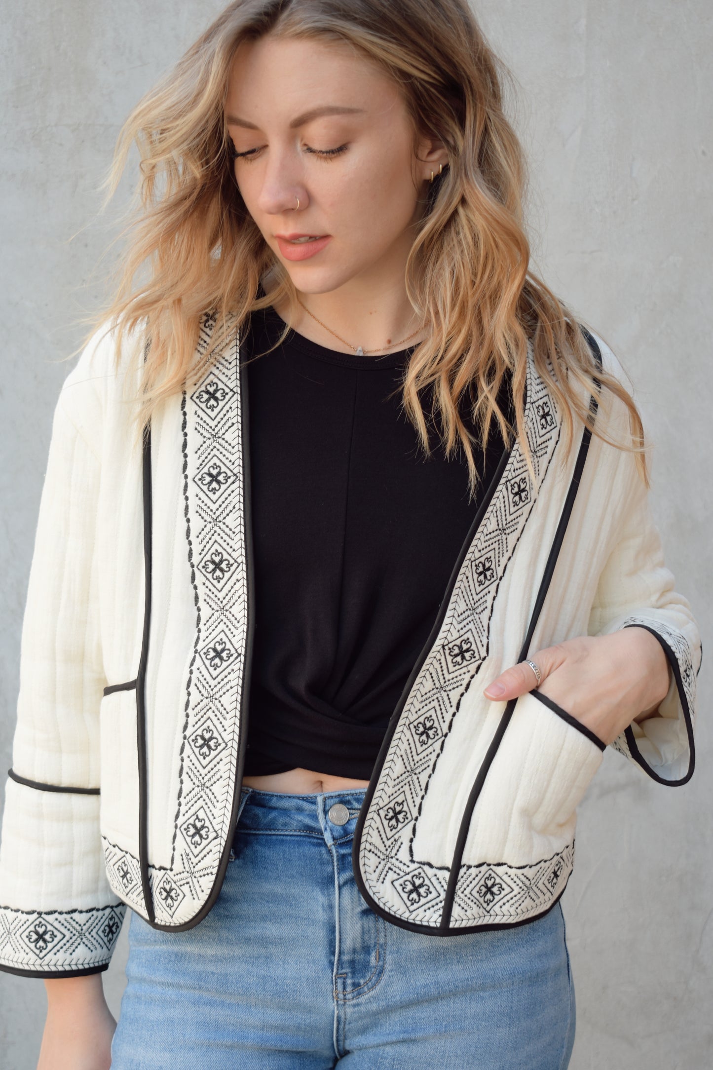 boho quilted ivory jacket with black exposed seam detailing and design along hem, has pockets, 2 clasp enclosure 