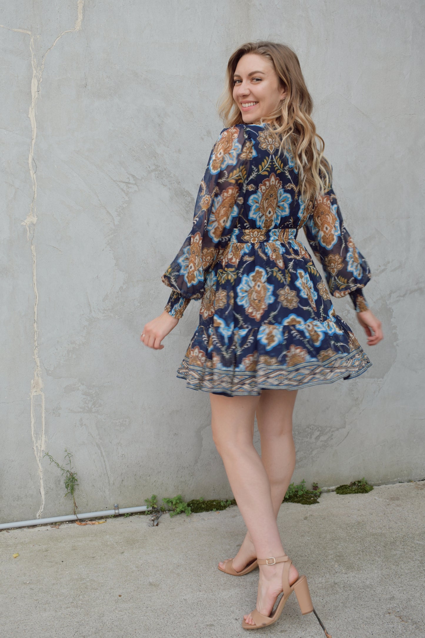 dark blue mini dress with gold, white, and light blue boho pattern. deep v neckline and waist yoke with long sleeves sinched at cuff. back zip enclosure. full skirt. chiffon fabric making sleeves look sheer.