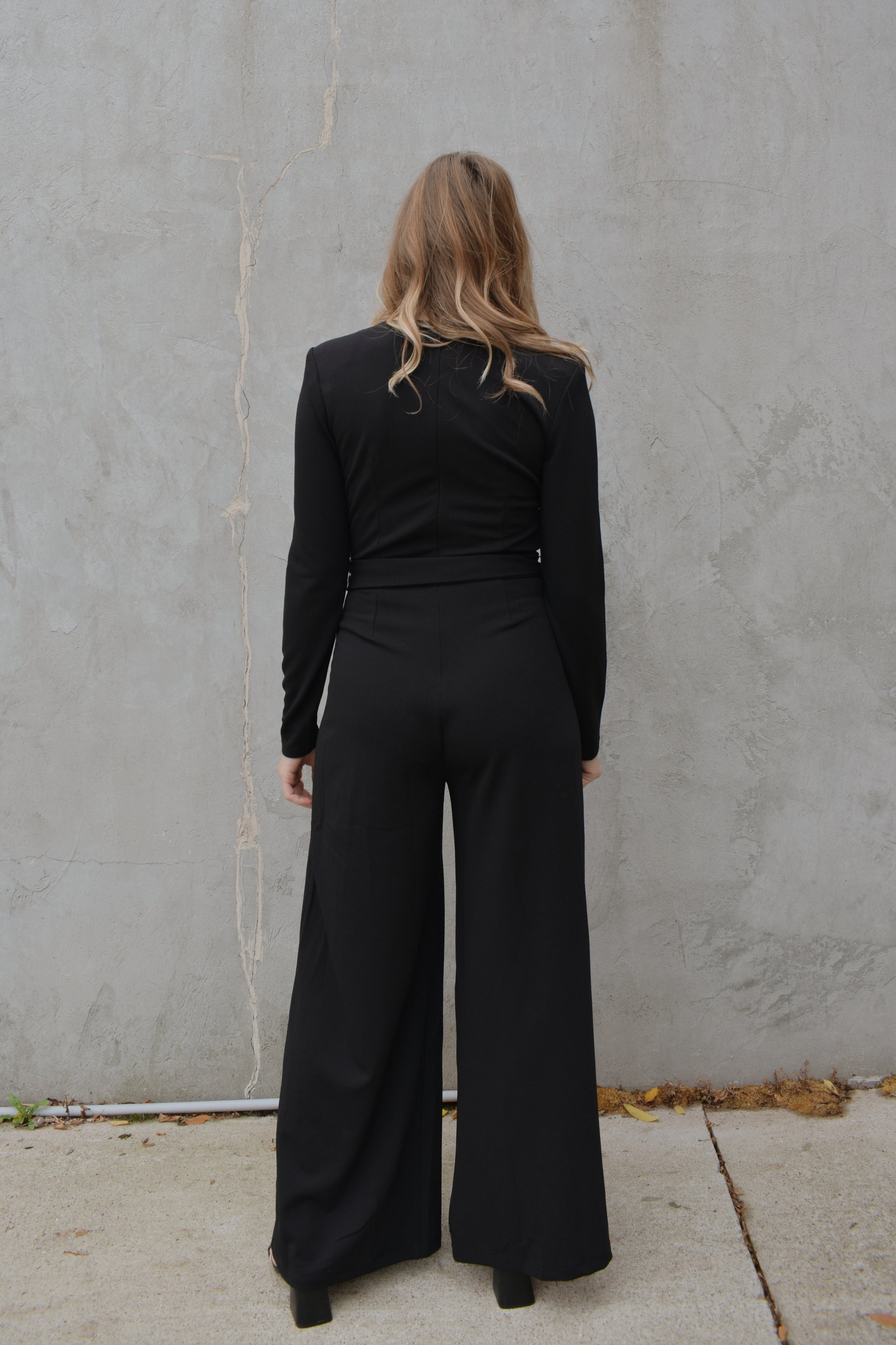 black wide leg long sleeve jumpsuit with wrap effect and fabric tie. pleated v neck with fitted arms and zip back enclosure