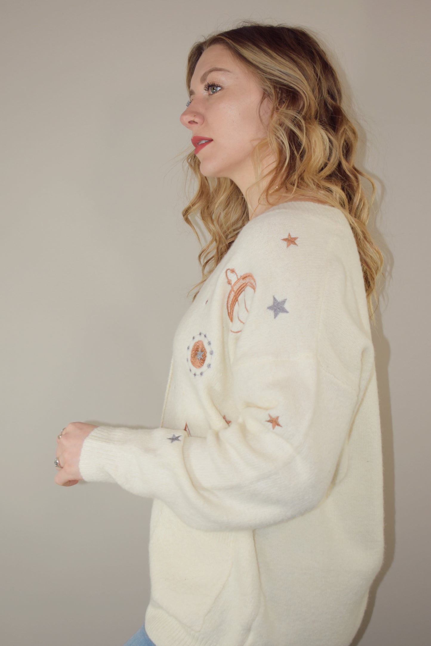 cream slouchy v neck button down cardigan hits just below hips and is embroidered with stars moons and suns has front patch pockets and drop shoulders