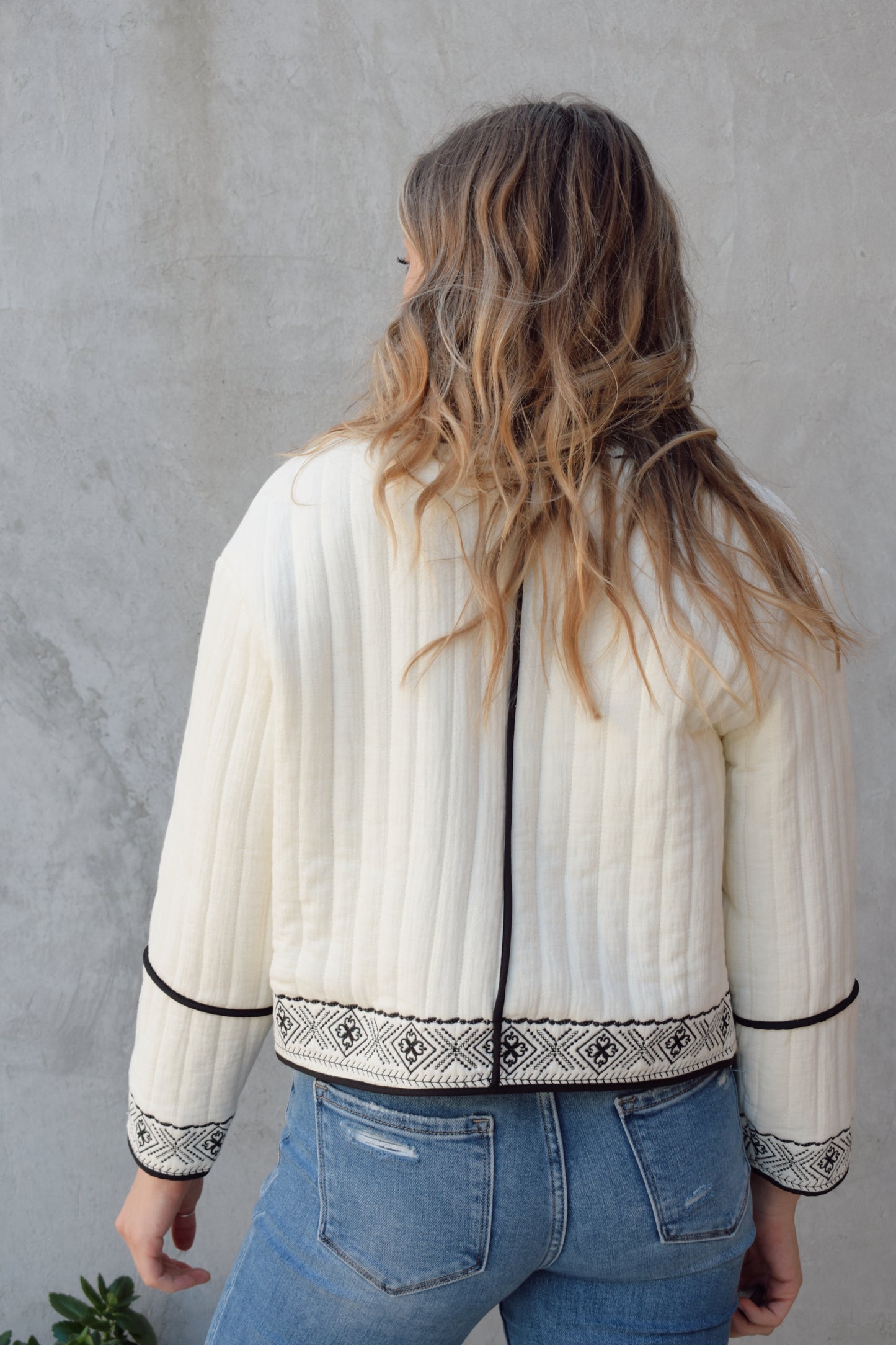 boho quilted ivory jacket with black exposed seam detailing and design along hem, has pockets, 2 clasp enclosure 