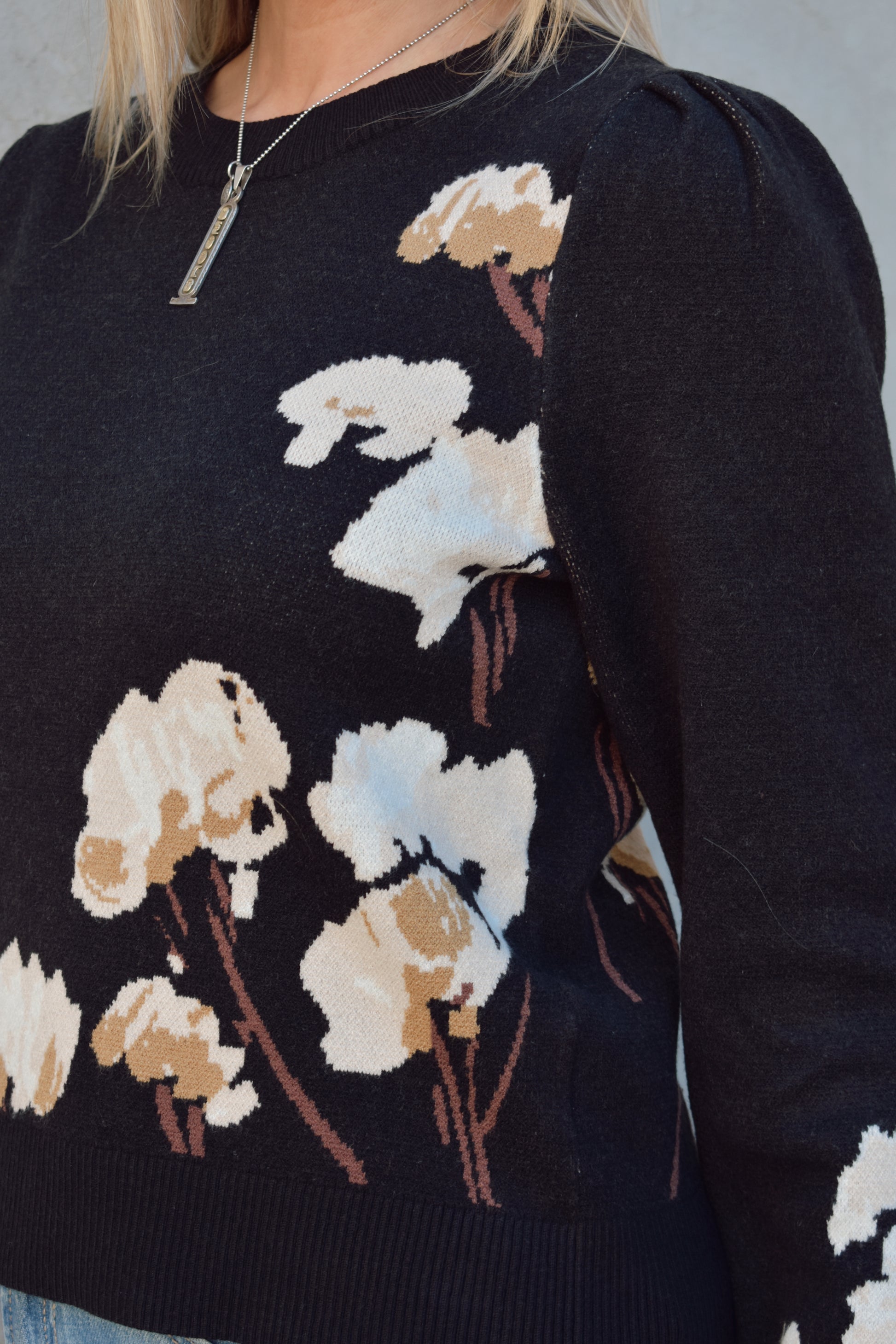 black sweater with cotton flower design on the left side and on lower part of the sleeve in cream and brown colors. slight balloon sleeve effect at shoulders. slightly cropped hem. round neck.