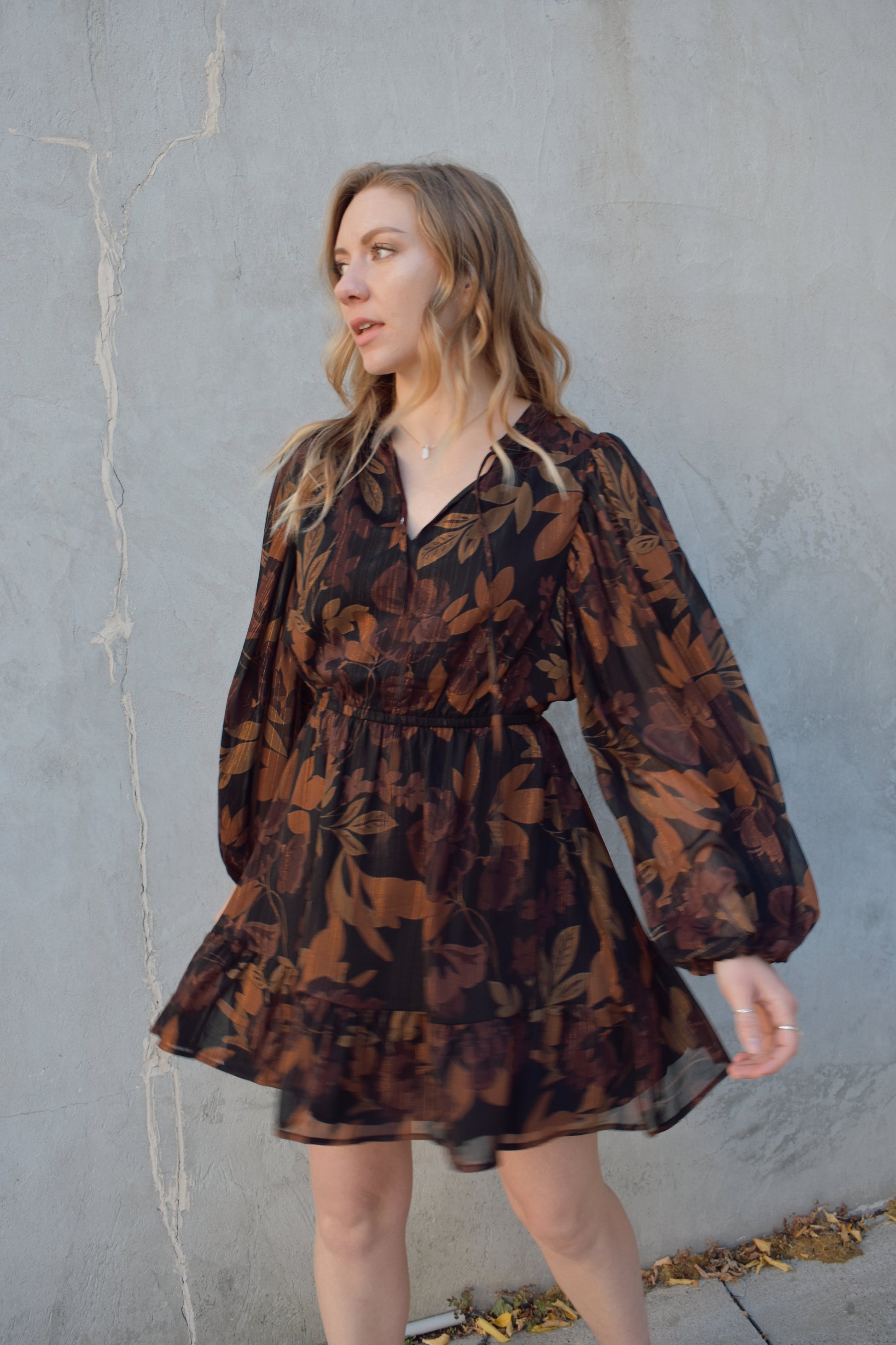 long sleeve chiffon mini dress with leaf print. black background with shades of brown in print. gold tread throughout. sheer balloon sleeves. split v neckline with tie, elastic waist, tiered just above hem making it swing and flowy. lined.