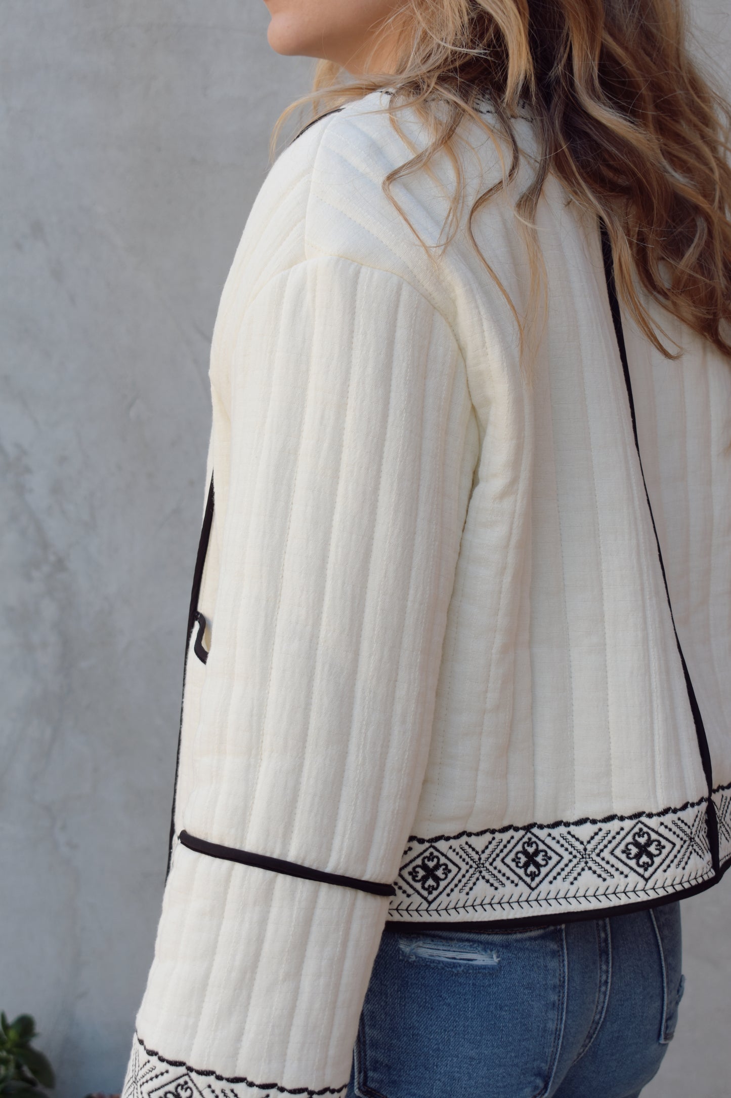 boho quilted ivory jacket with black exposed seam detailing and design along hem, has pockets, 2 clasp enclosure 