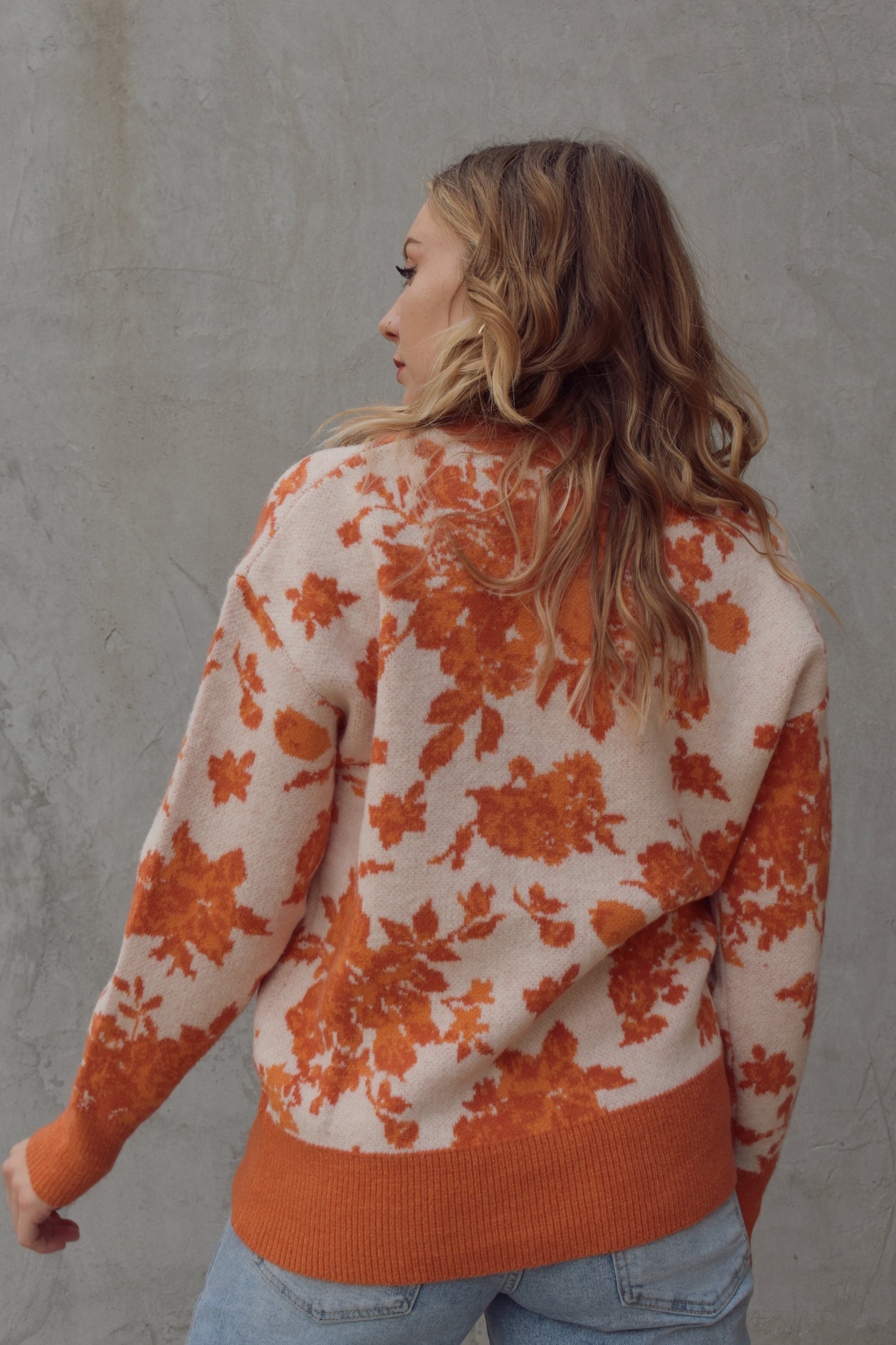 ivory and shades of orange high neck sweater with a leafy floral design. hemline neckline and cuffs are solid orange and ribbed. full length, relaxed fit, drop shoulder.