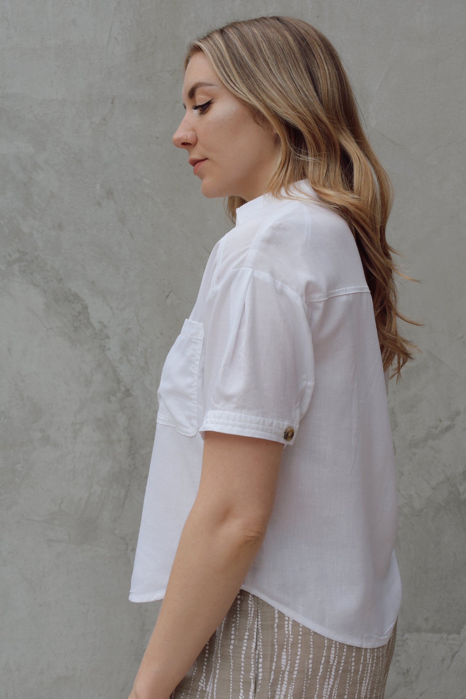 white linen button down, short sleeve, v neck with collar, 3 brown buttons, patch breast pockets, scoop hemline, button detail on back of sleeve cuff