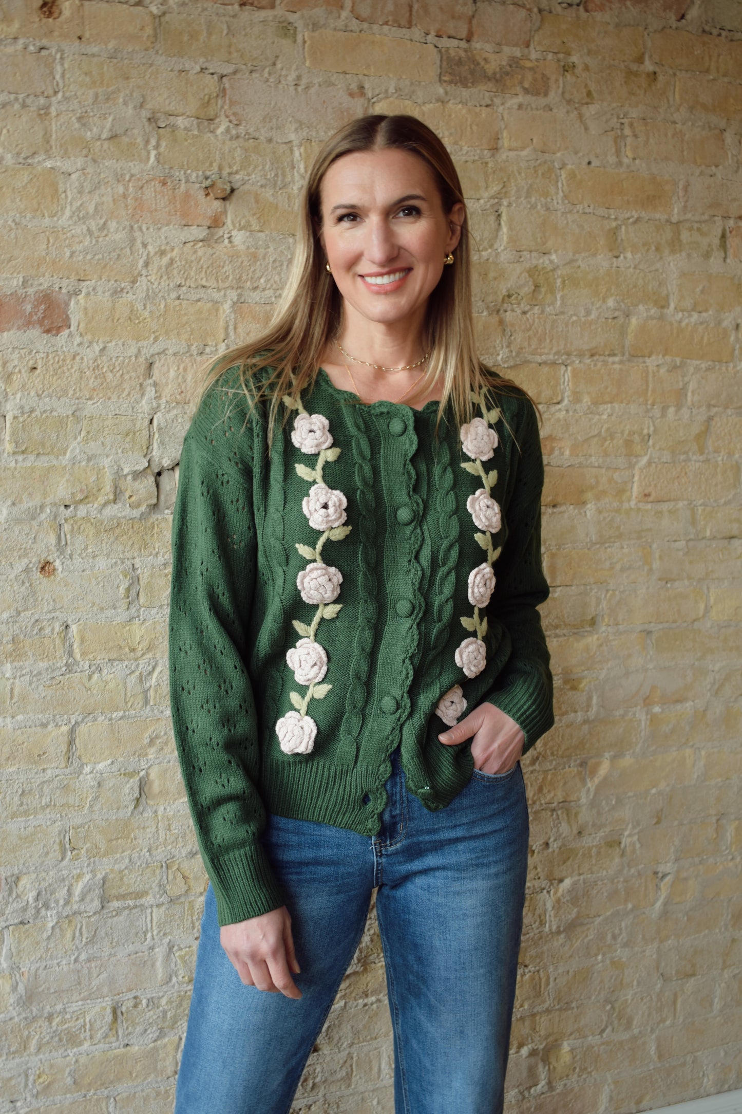green cable knit cardigan with scalloped neckline, light pink flower crochet detailing along front ribbed cuffs and hem, hip length, relaxed fit