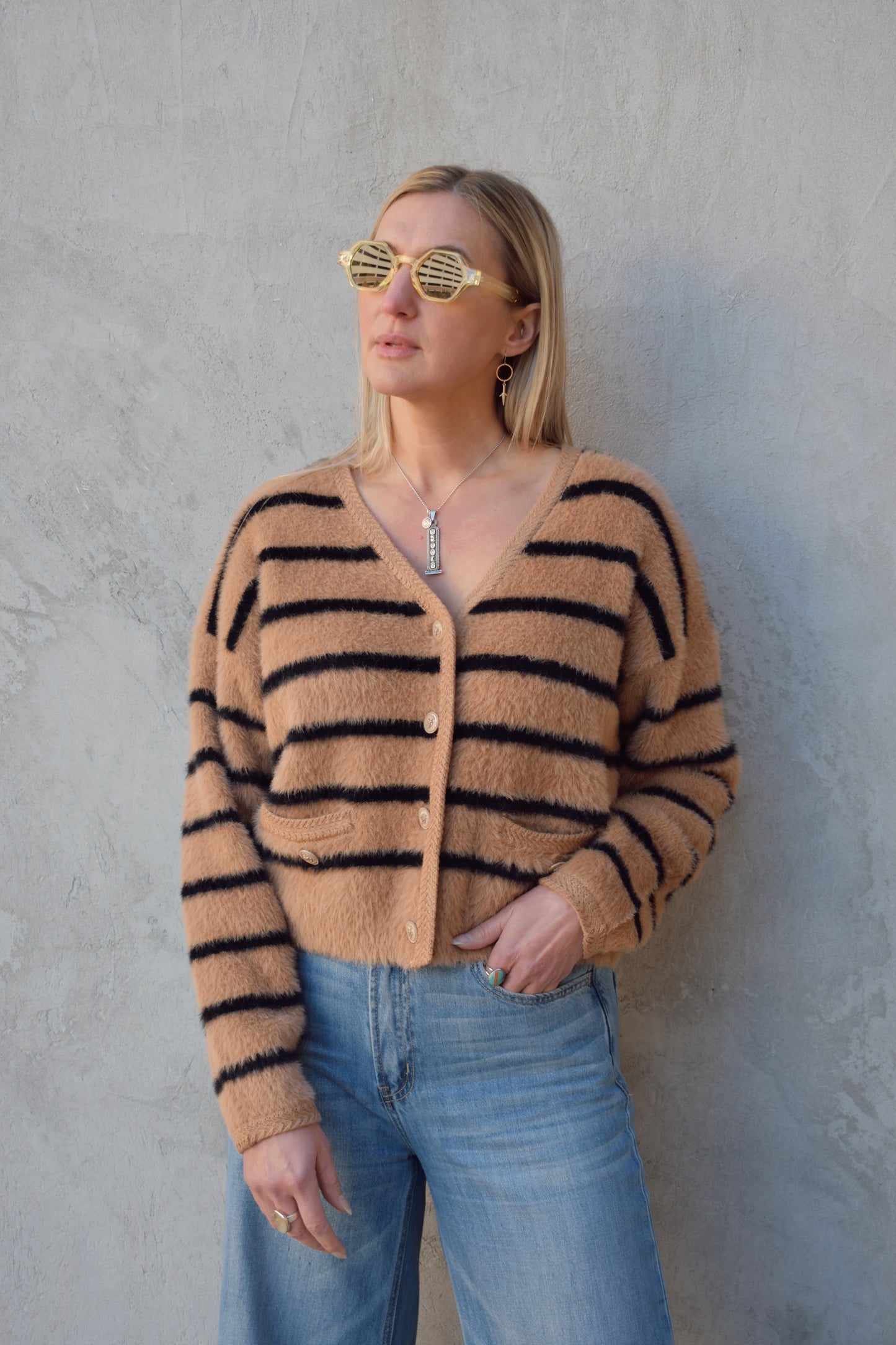 light brown mohair v neck button down cardigan with light brown sailor buttons and black horizontal stripes. two pockets on front that open at the top. outlined with a braided texture on neck line and down the front and on edge of pockets. drop shoulders, slightly cropped.