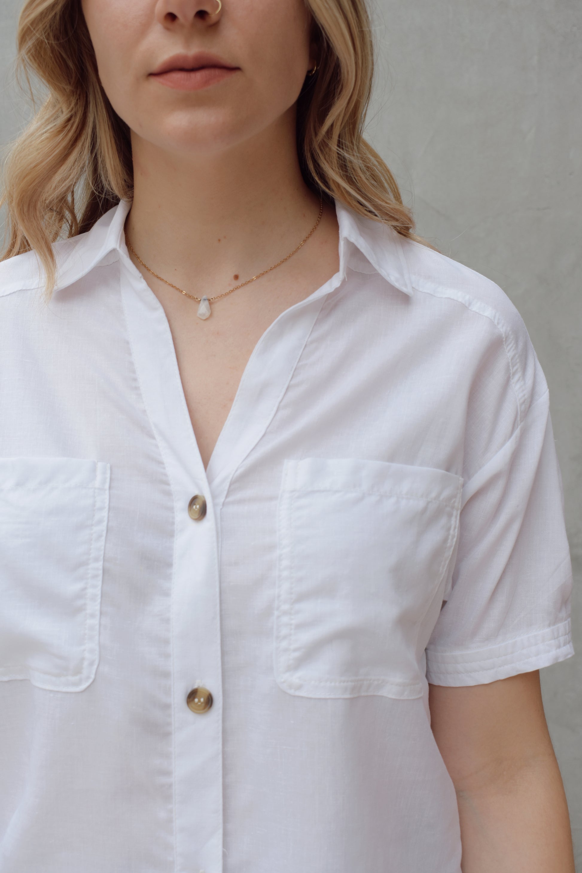 white linen button down, short sleeve, v neck with collar, 3 brown buttons, patch breast pockets, scoop hemline, button detail on back of sleeve cuff